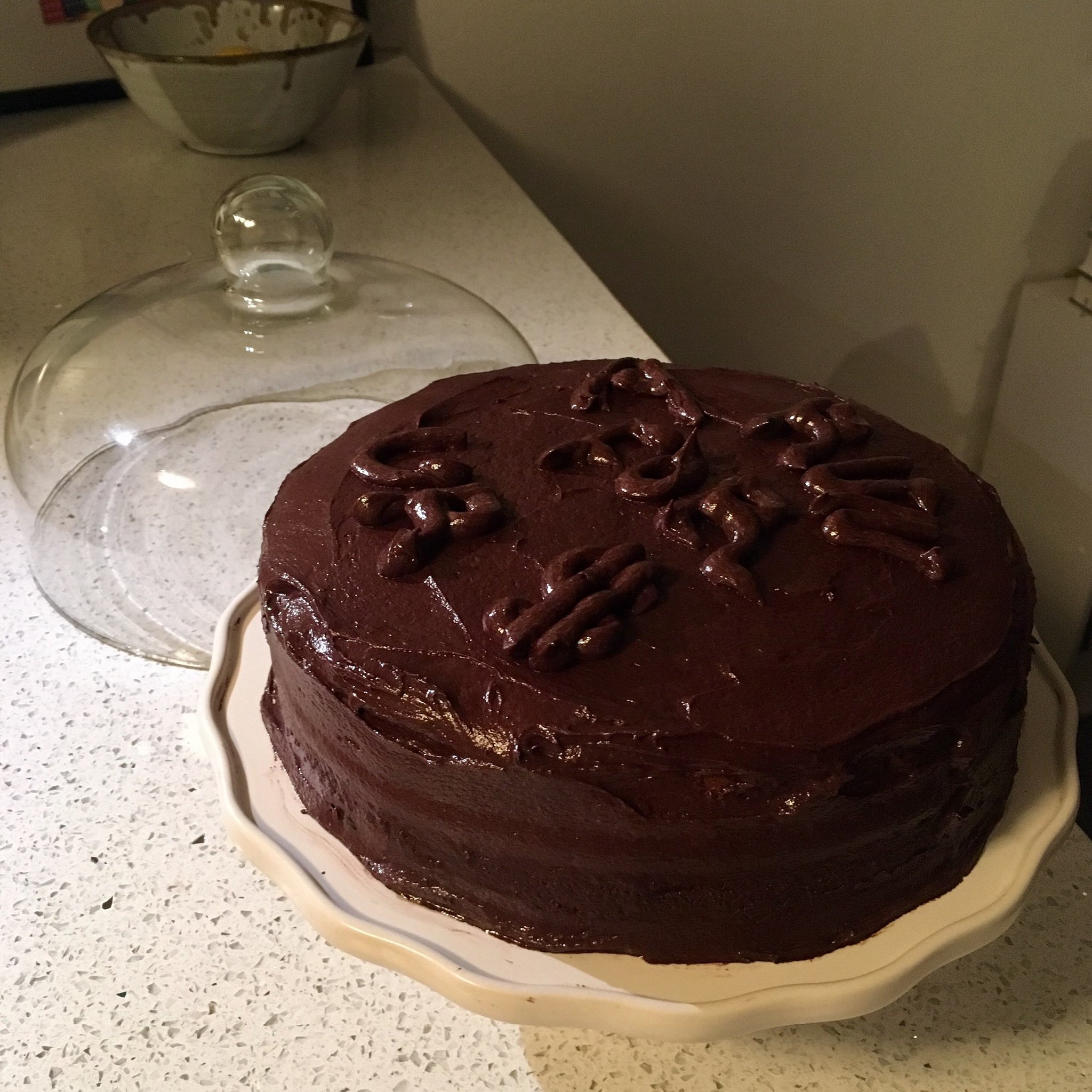 A chocolate-frosted cake on a cake stand with the phrase "A RUN FOR UR $" iced in frosting.